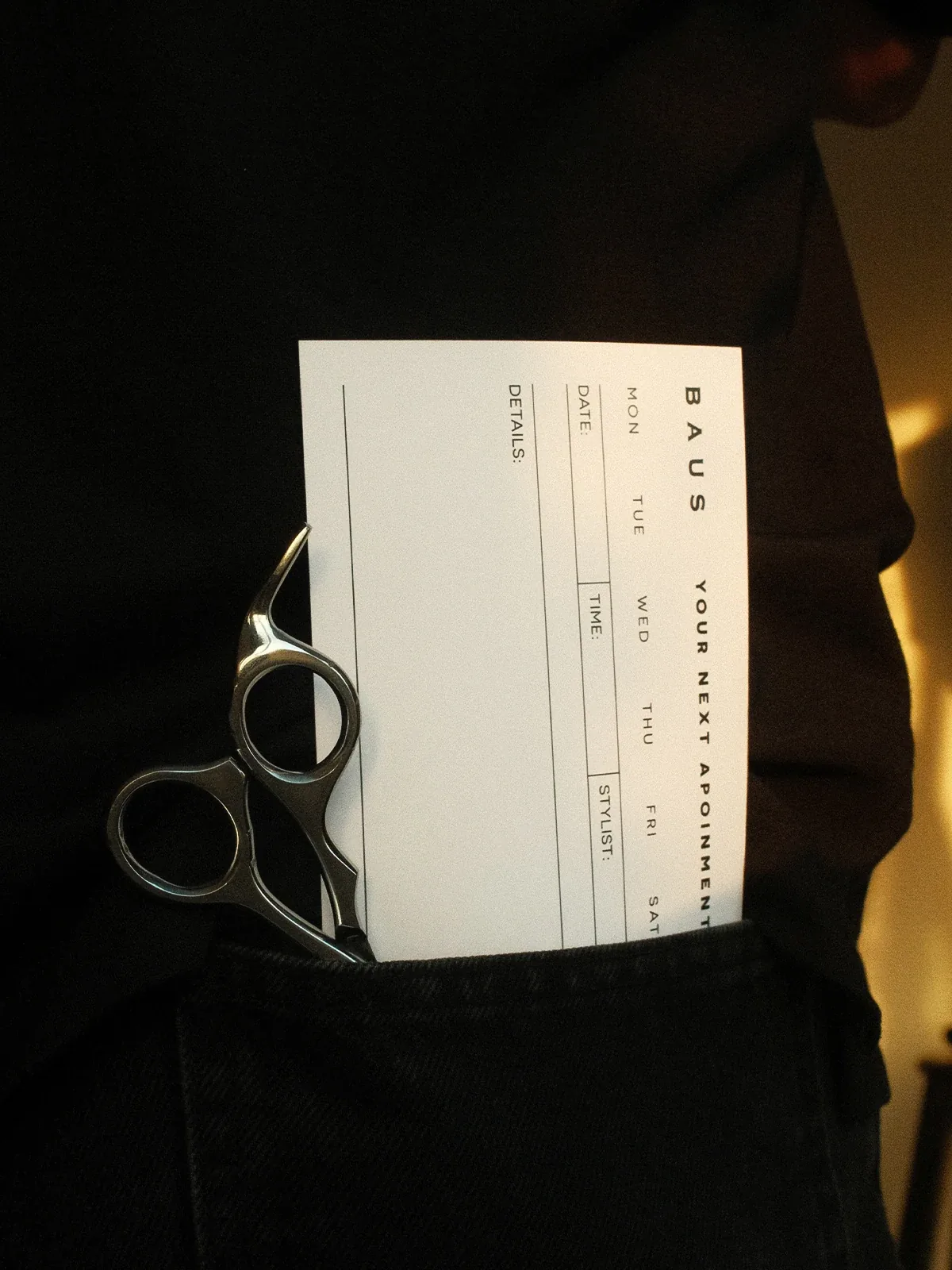 Baus appointment card tucked in a barber's apron pocket with scissors