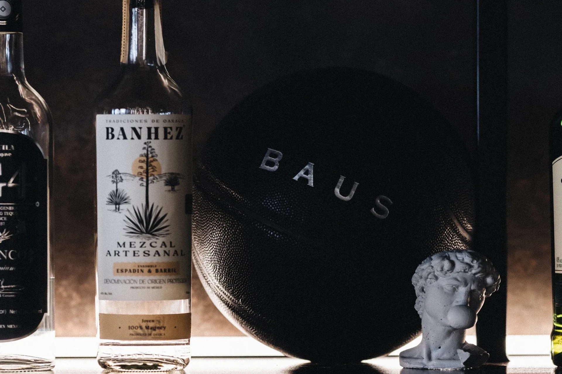 Black Baus tray beside a mezcal bottle and a classical bust